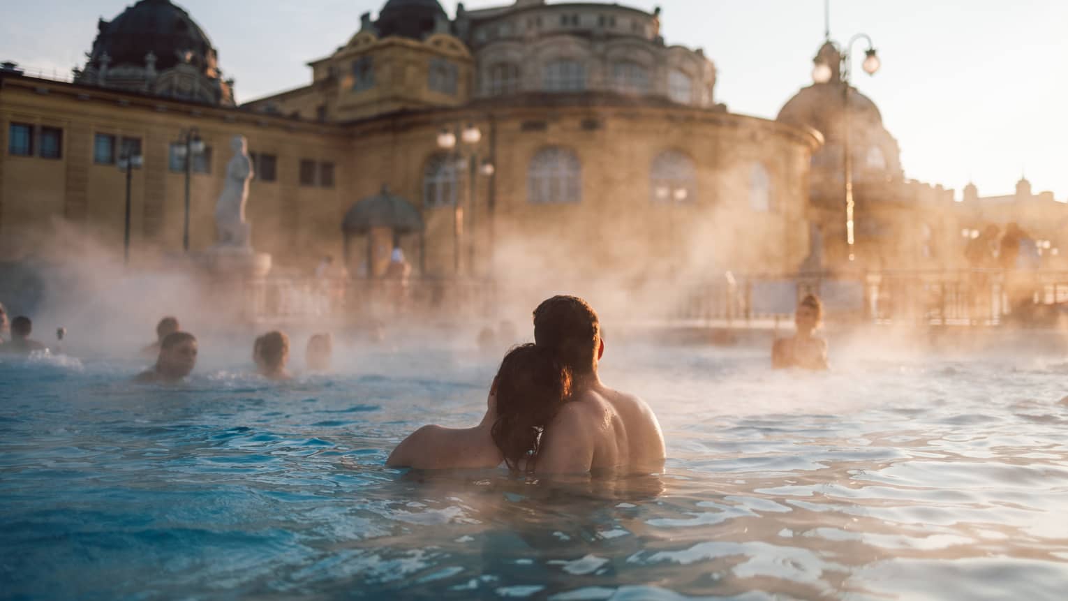 Couple huddled together in thermal pool at Szechenyi Thermal Baths in Budapest, other bathers in background