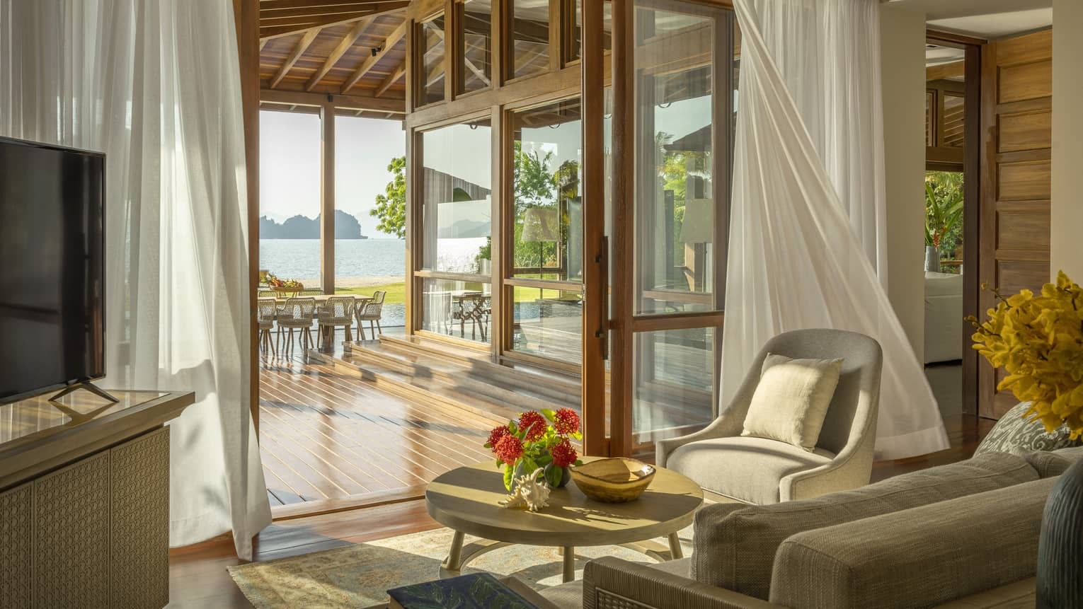 Sitting area opening up to covered wooden deck with beach view