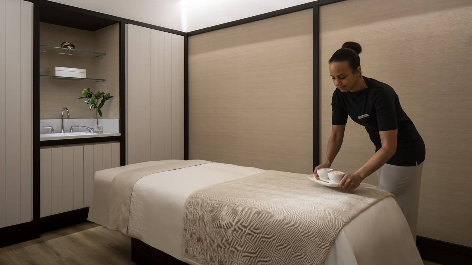 Spa staff places small dish on massage bed in couples suite