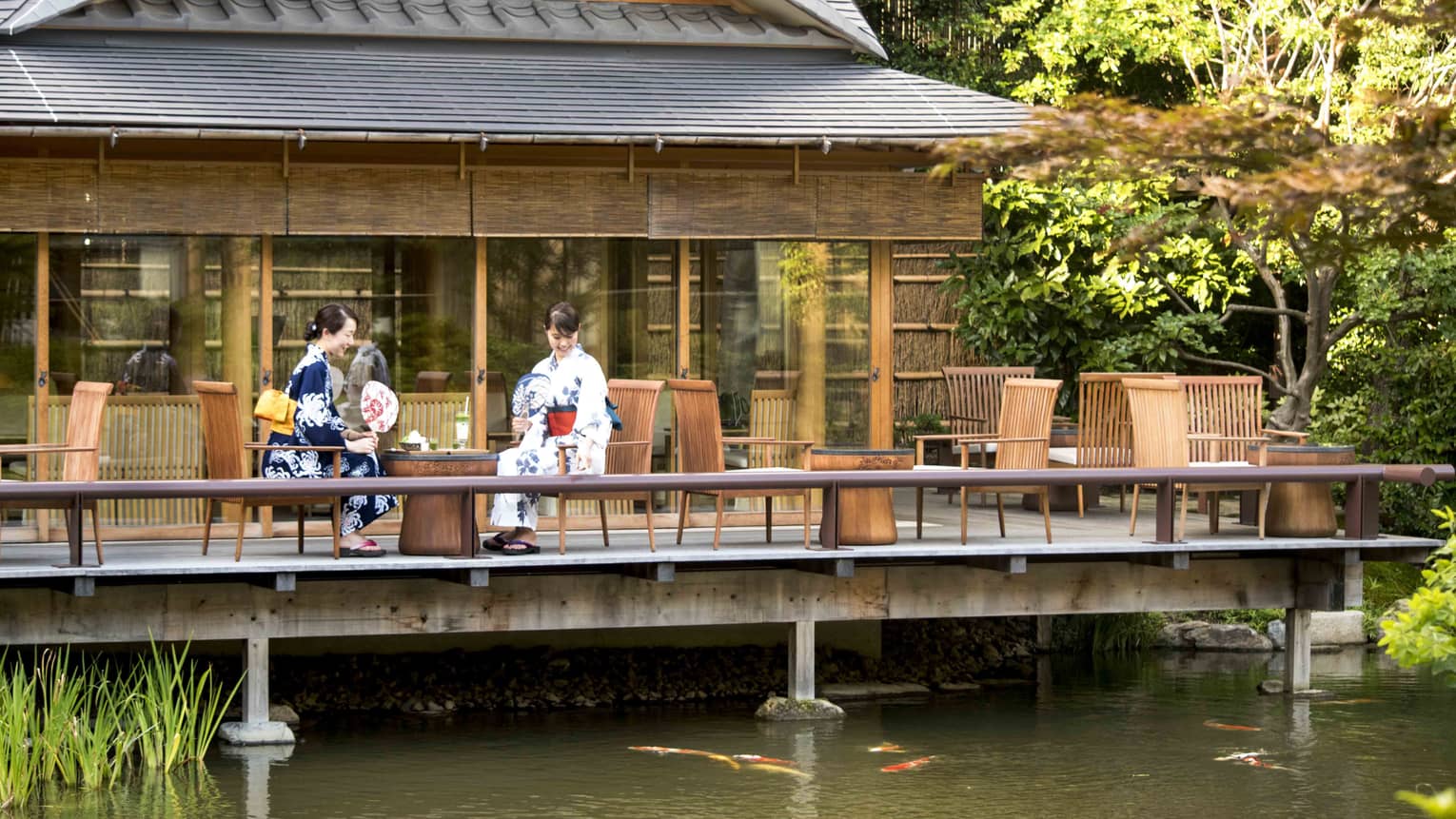 Two women in traditional Japanese garb observing the koi fish swimming below