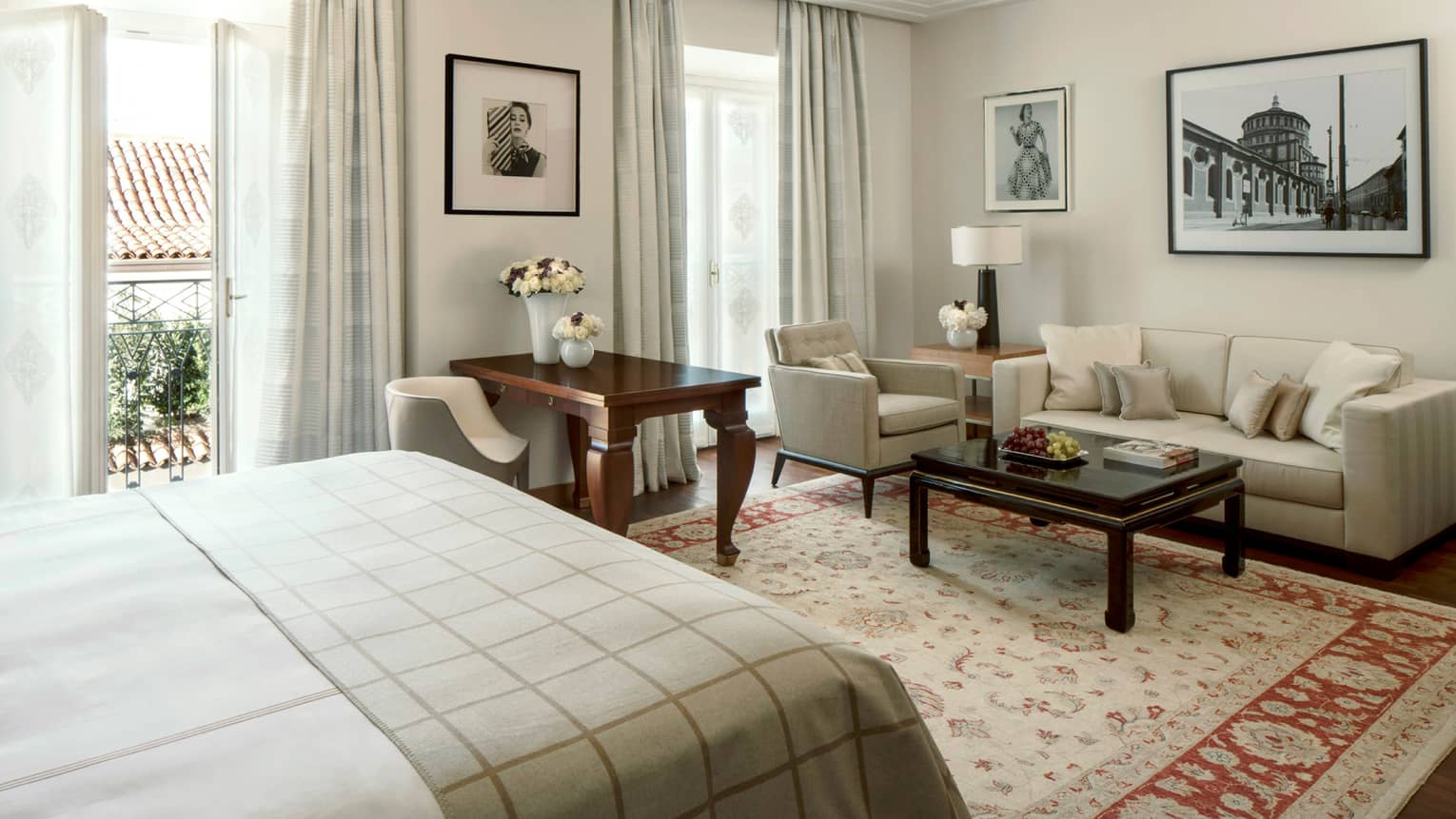 Four Seasons Executive Suite bed with checkered blanket, wood desk, seating area under black-and-white prints