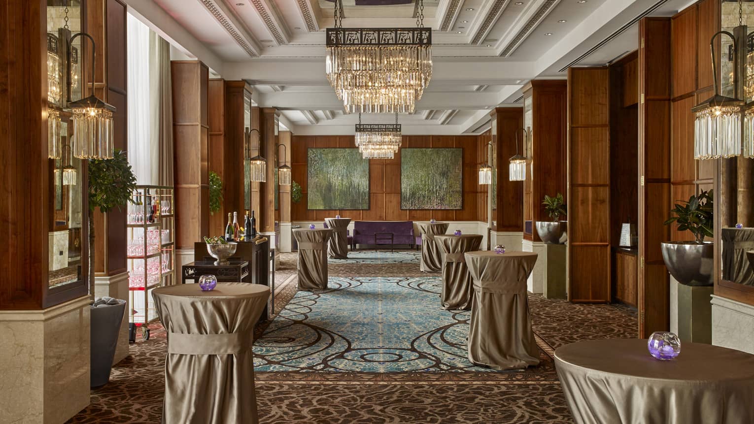 Room with large chandelier, drinks tables covered in tablecloths, bar with drinks