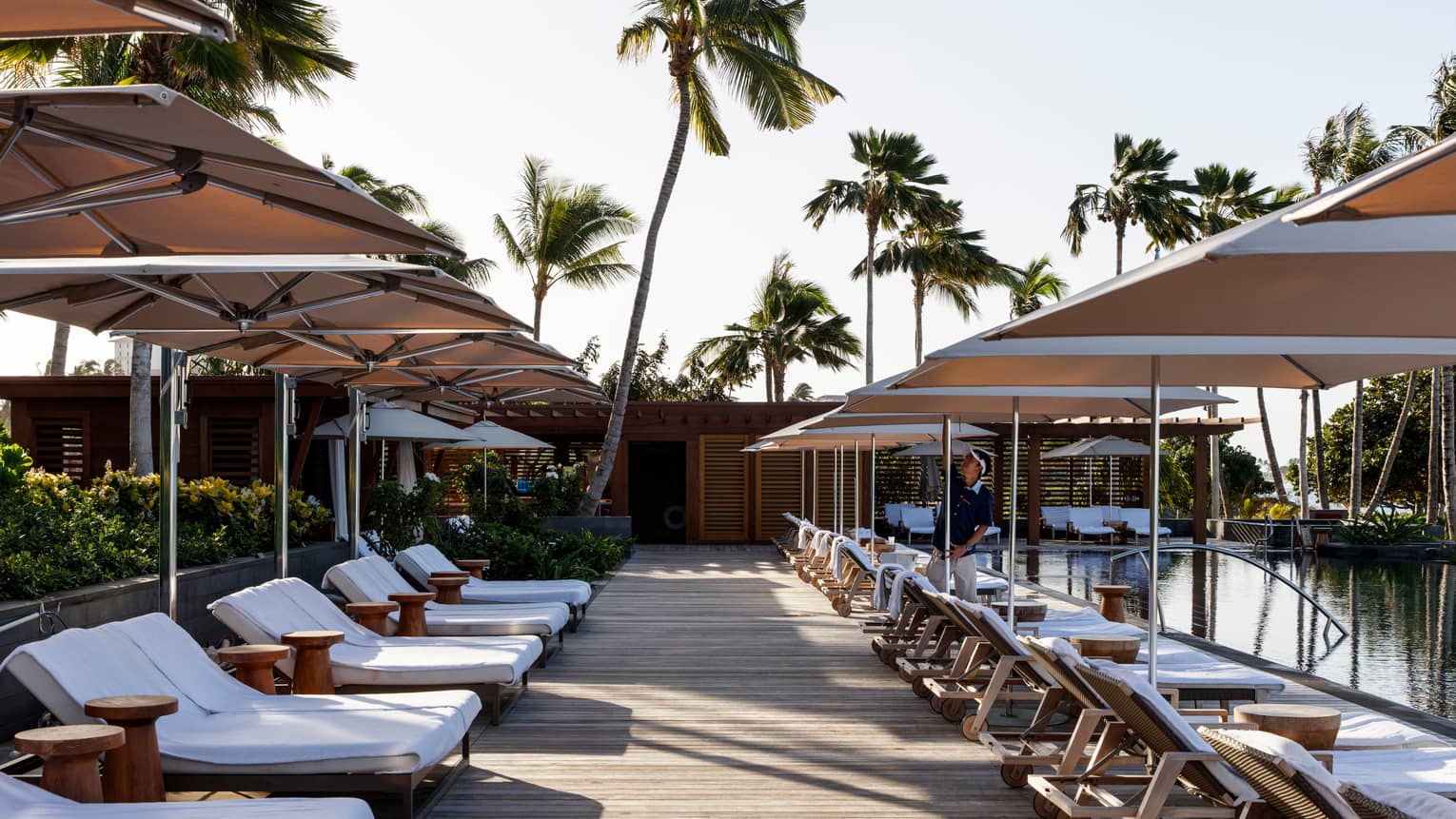 Rows of white lounge chairs, patio umbrellas over outdoor pool deck
