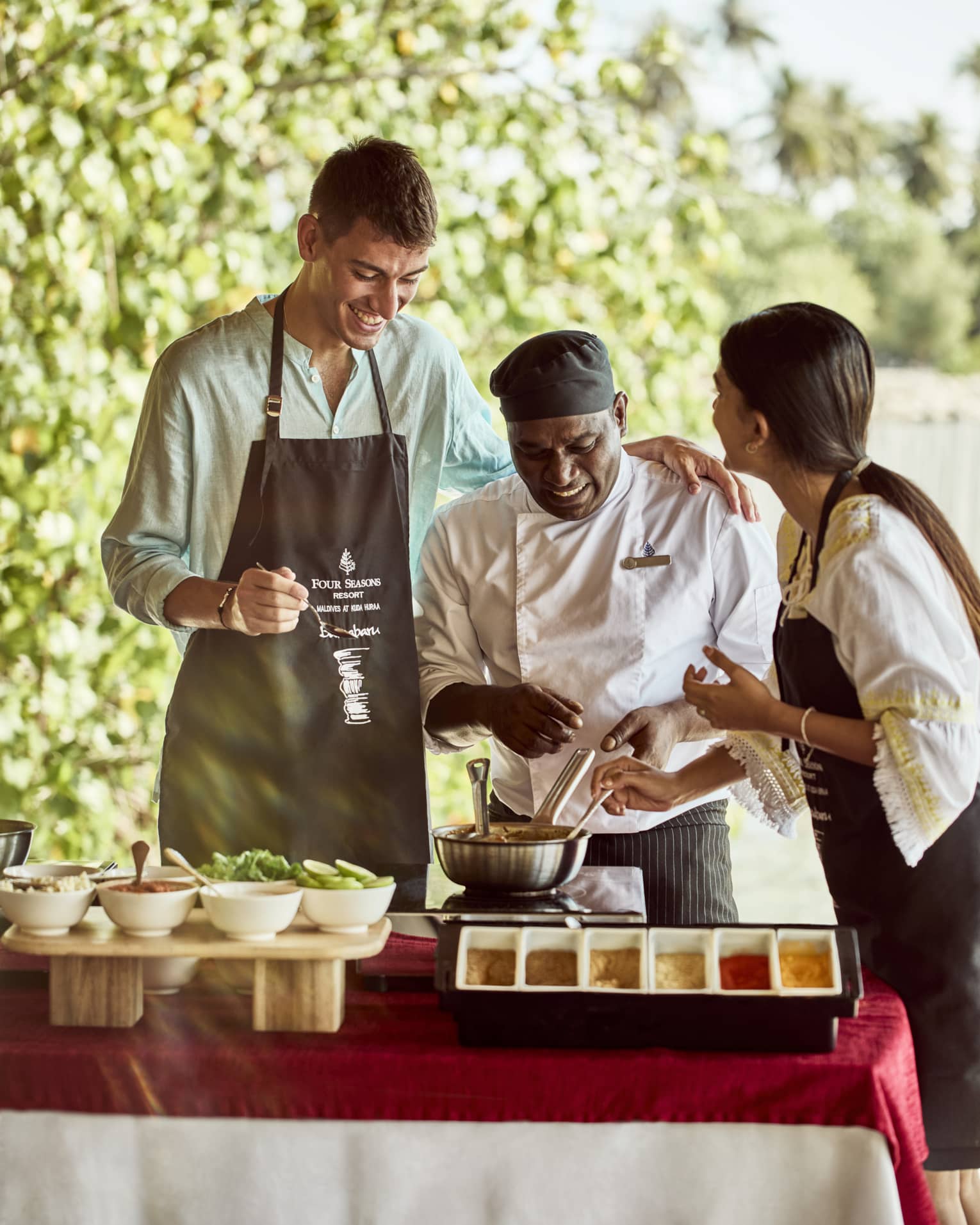 Chef teaches two guests how to make traditional Indian dish in outdoor kitchen