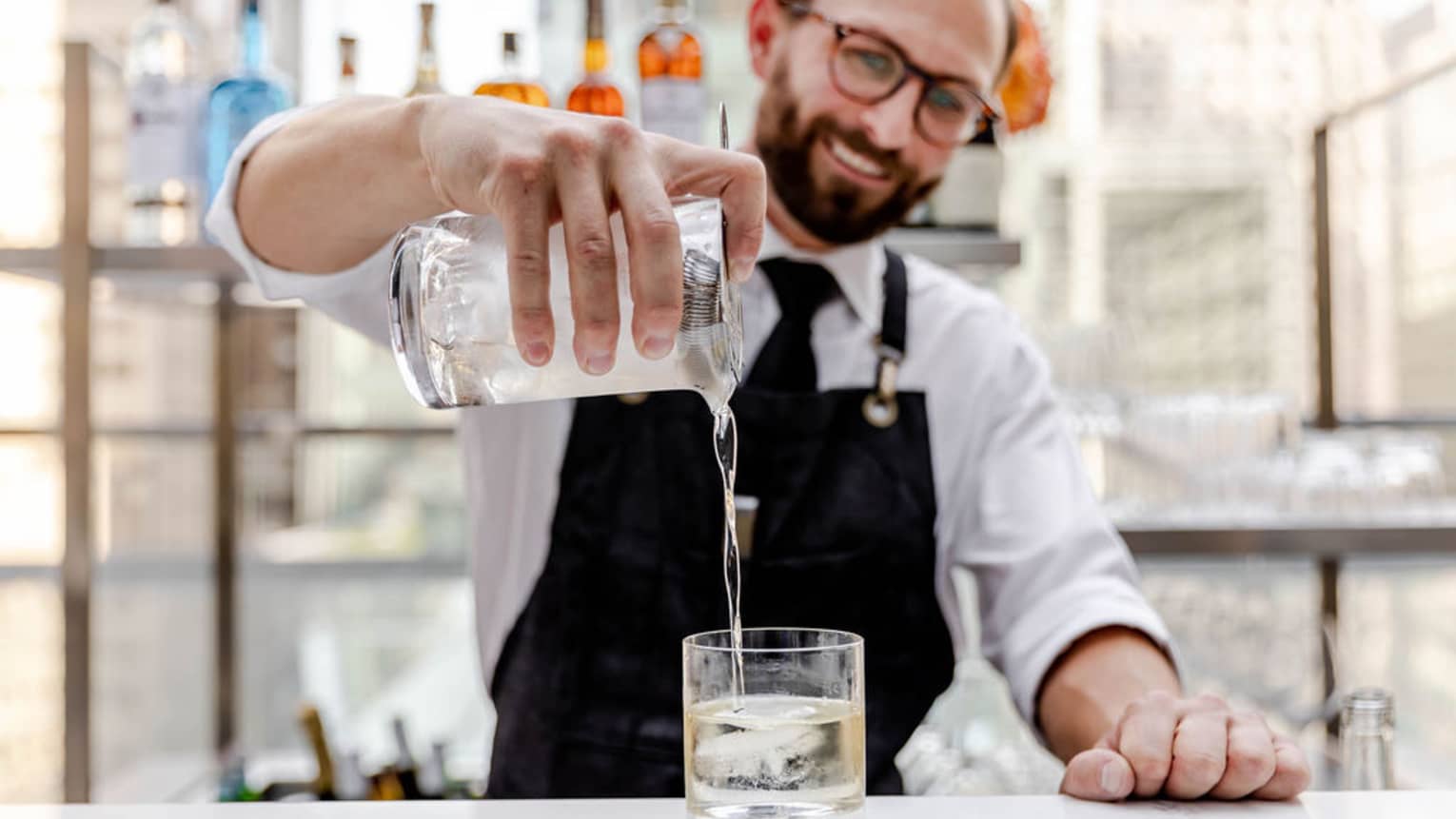 A bartender pouring a drink into a glass.