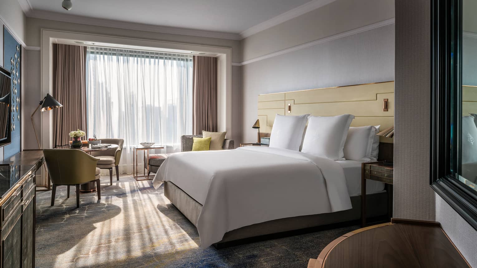 Sunny Premier Room bed with white linens, small dining table and chaise lounge, white curtains