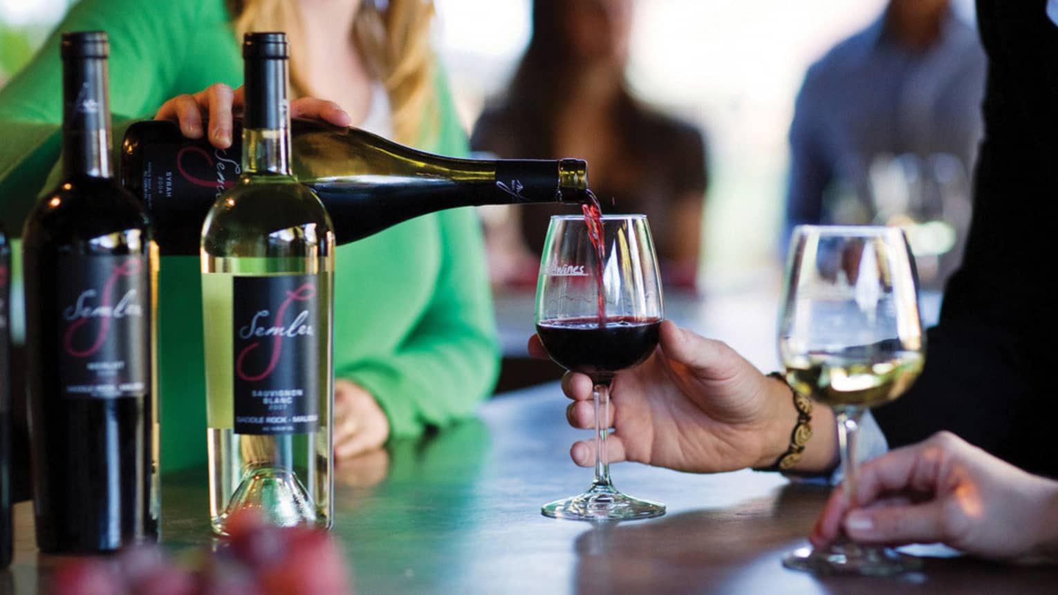Woman pours red wine from bottle into glass at Malibu Coast tasting bar