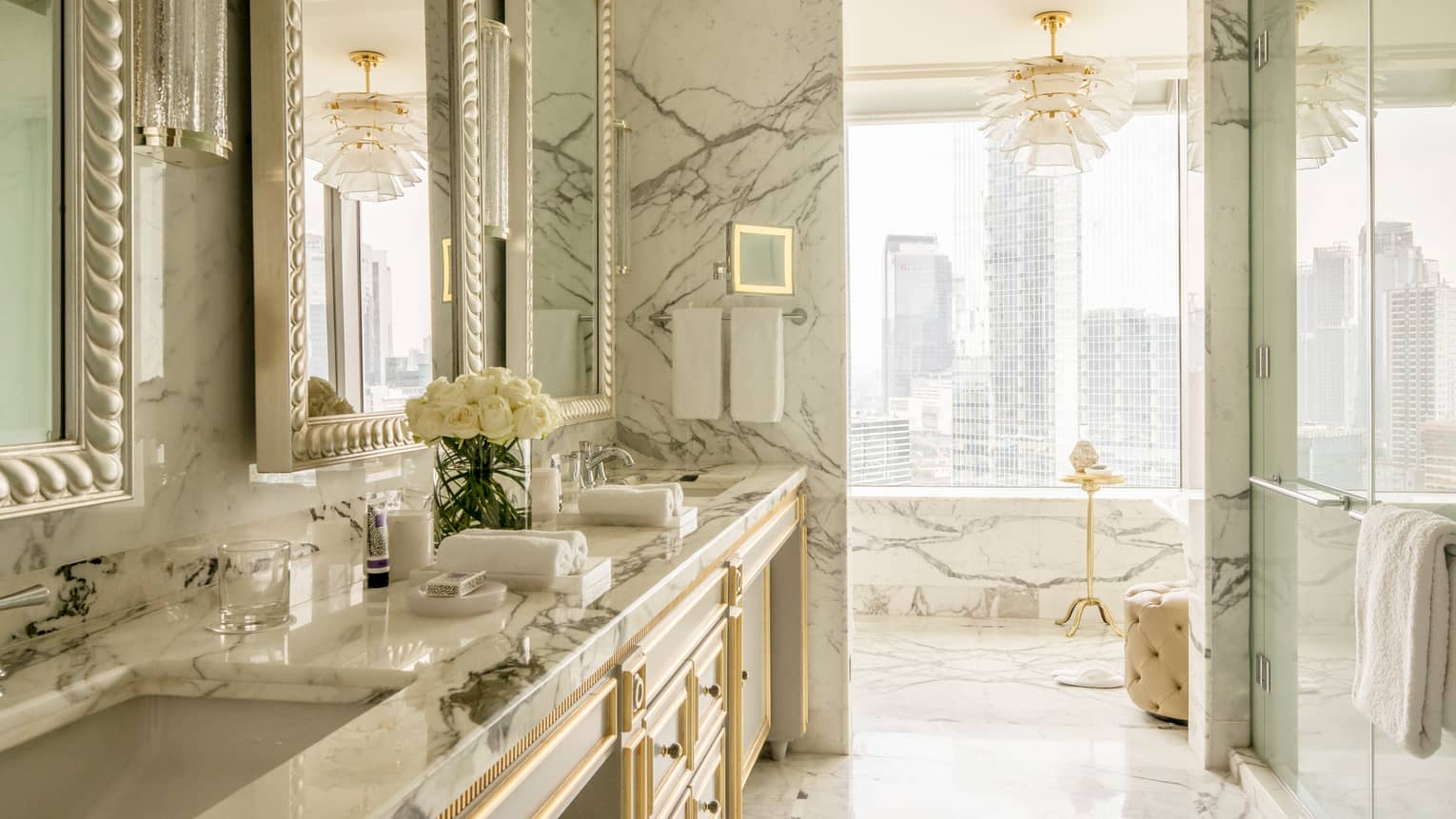 Presidential Suite bright white marble bathroom with double sink, glass shower, white chandelier, city views