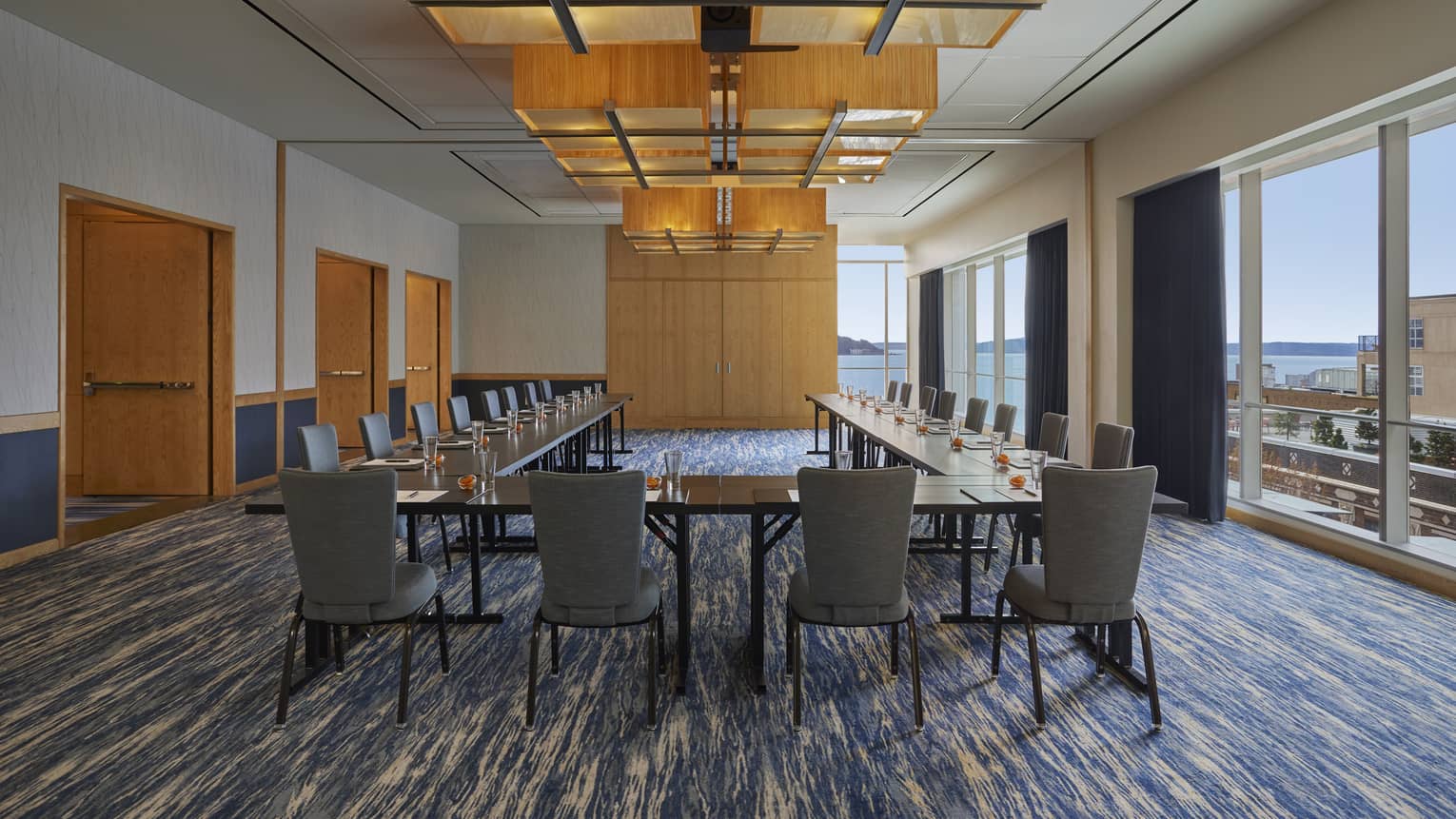 A room with a large U-shaped table, many chairs and large windows.