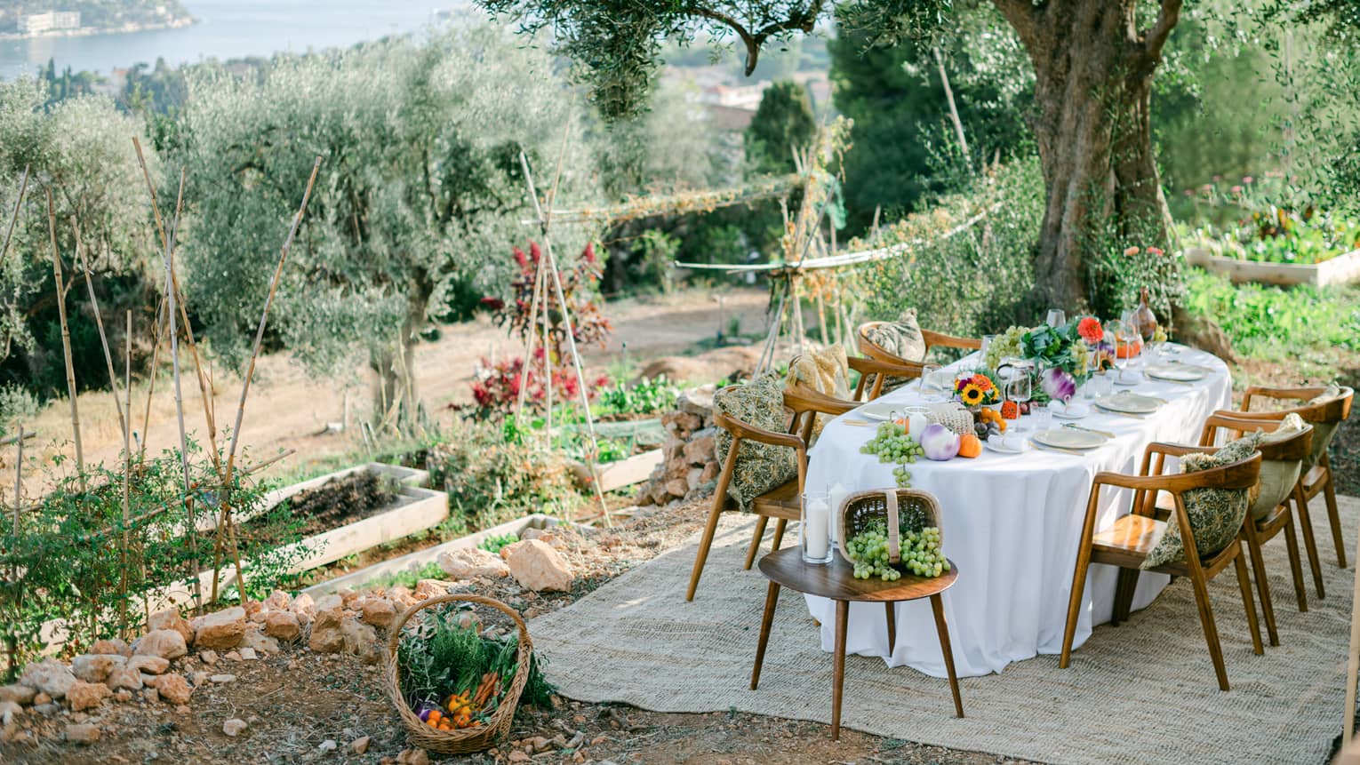 Garden dining setup with oval table draped in white and garden bounty down centre, and six chairs with pillows