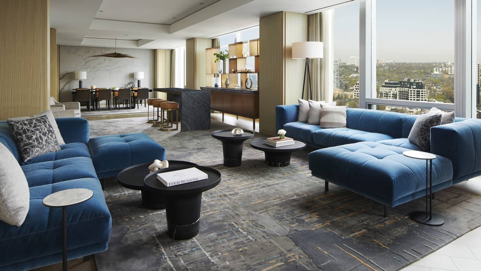 Living room with two large blue sofas, wall of windows, dining room in distance