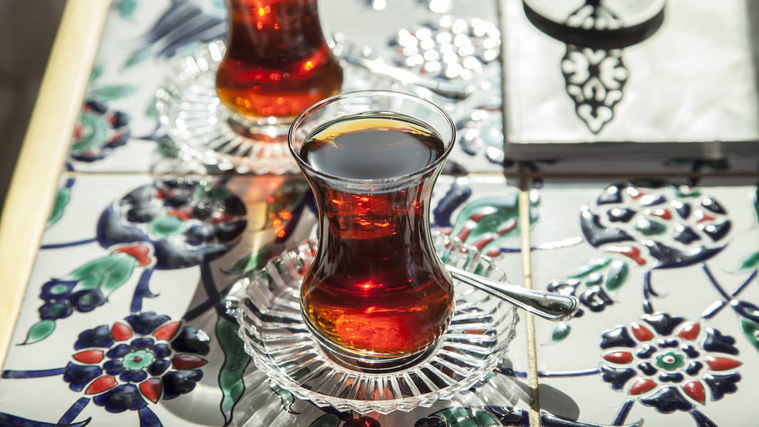 Two Turkish Tea glasses with red tea on saucers on floral mosaic tile table