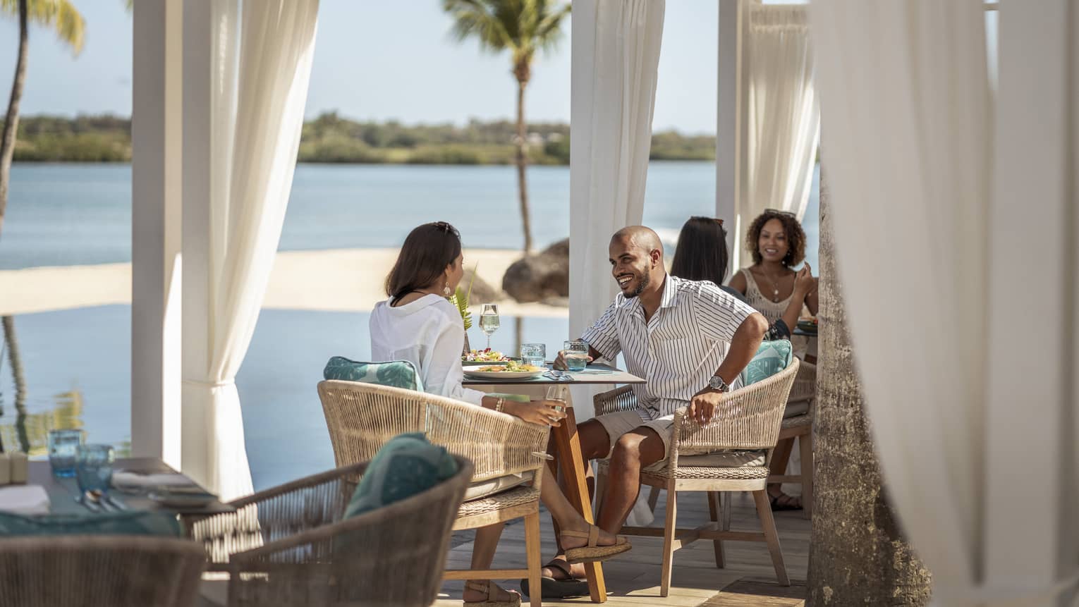 Couple sitting at waterfront restaurant, smiling over food and drinks 