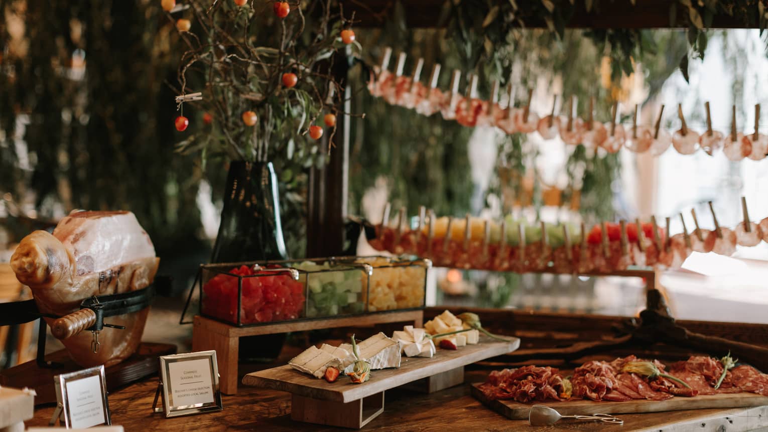 An assortment of food on wood trays with plants in the background.