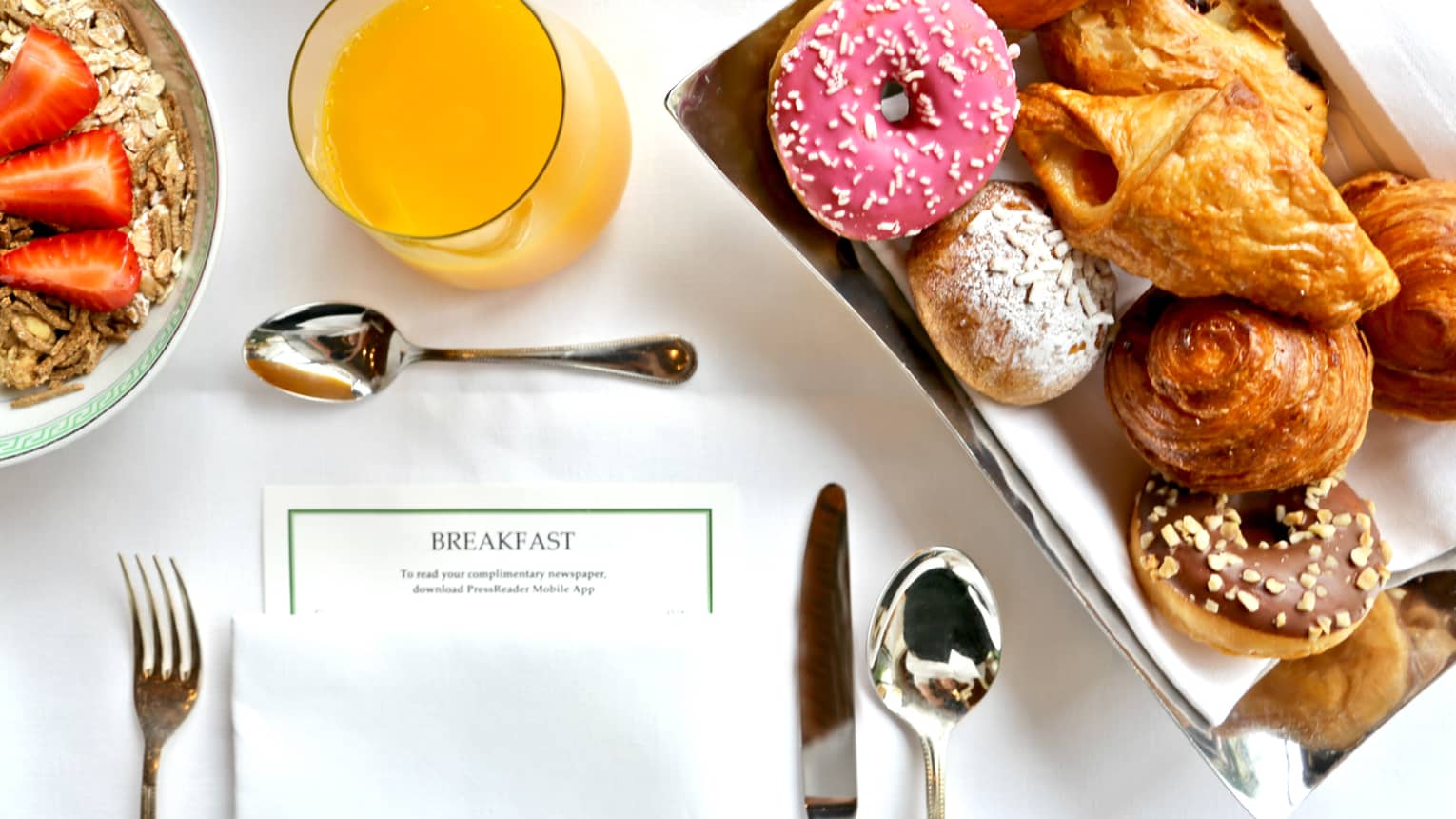 Aerial view of in-room breakfast table with menu, tray with pastries, doughnut with pink icing, orange juice