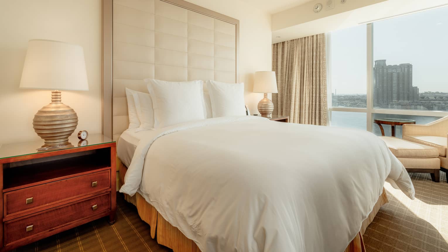 A guest room with floor-to-ceiling windows, two side tables with lamps and a view of the city