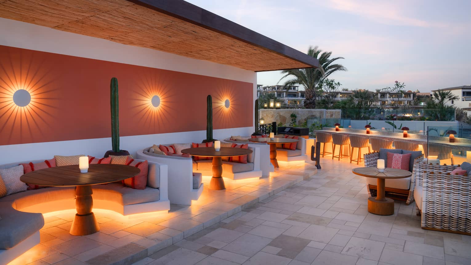 Rooftop bar at twilight with booth seating and a bar counter all light up with lights underneath the seats