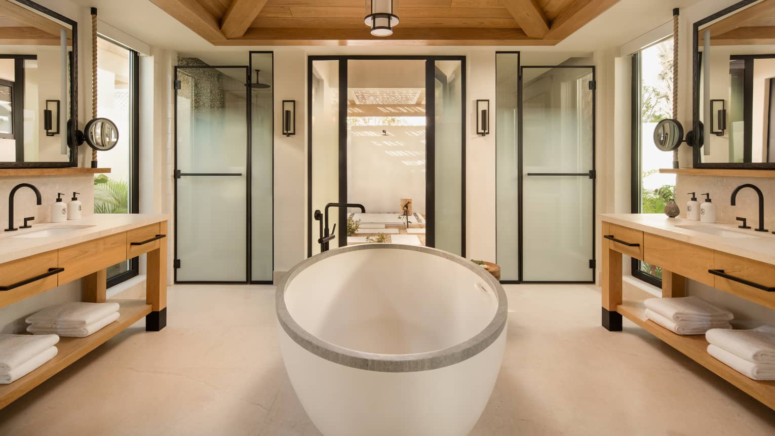 Large luxury bathroom with standalone oval tub in the middle, a vanity on each side, and a vaulted wooden ceiling