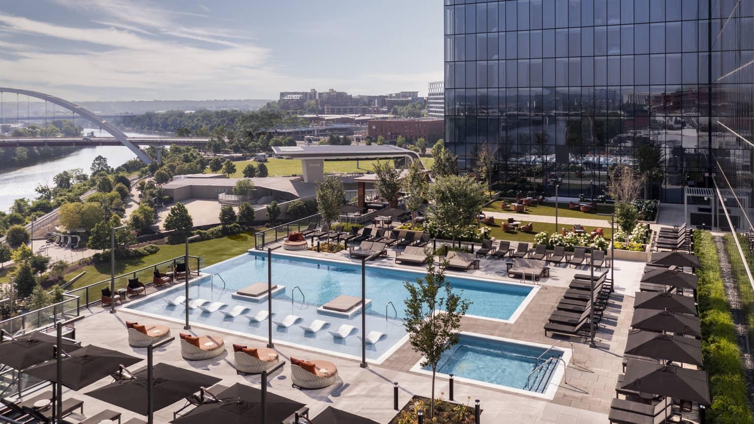 A rooftop infinity-edge pool at Four Seasons Nashville, surrounded by lounge chairs and cabanas, with views of the city skyline and greenery under a clear sky.,A rooftop infinity-edge pool at Four Seasons Nashville, surrounded by lounge chairs and cabanas, with views of the city skyline and greenery under a clear sky.