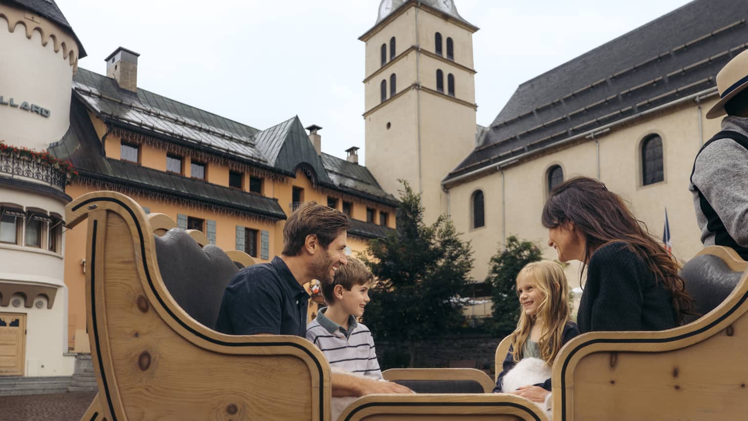 Family of four sitting in a horse-drawn carriage with historic building in background