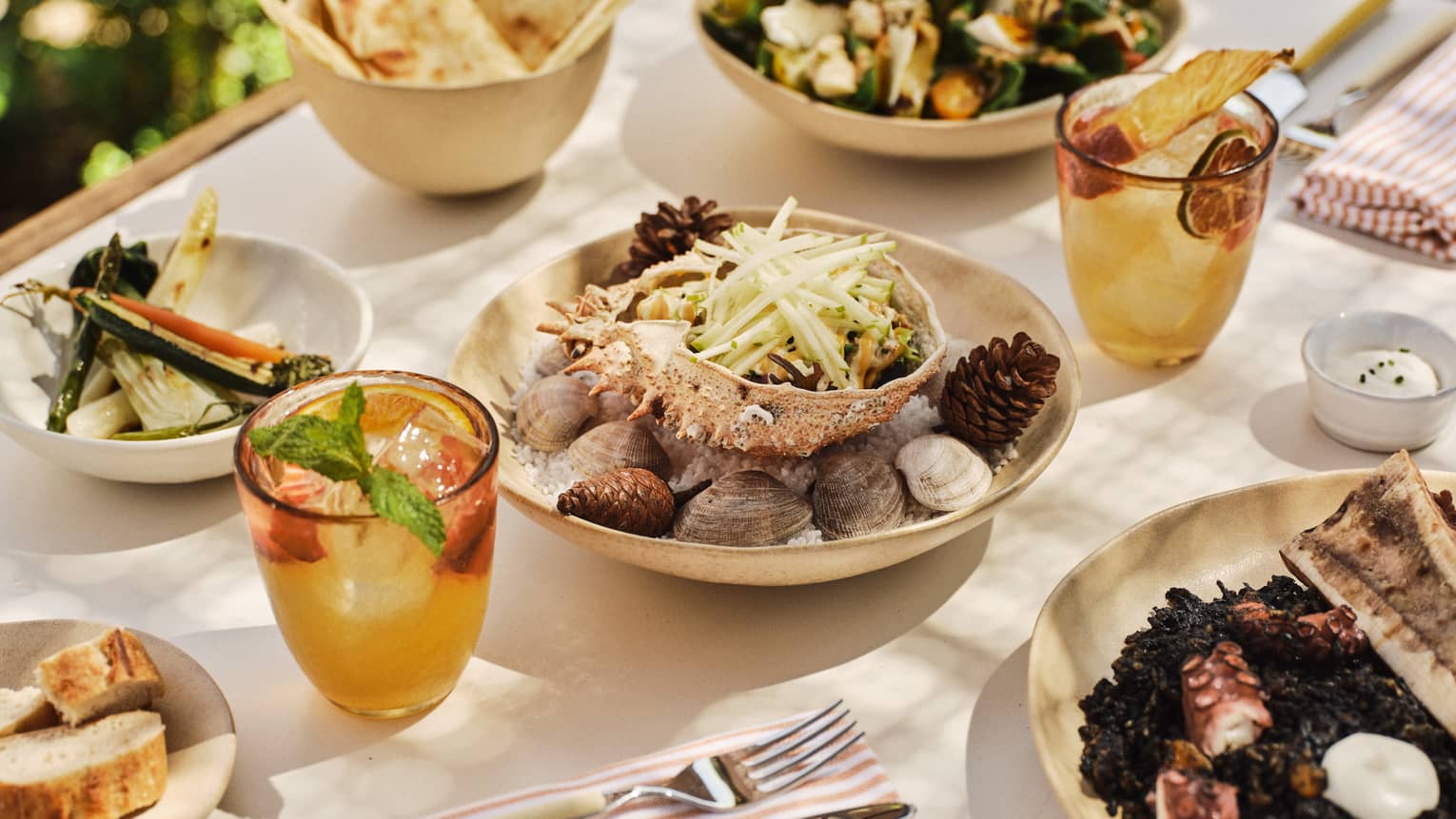 A variety of Spanish dishes set on a white-cloth table with two cocktails