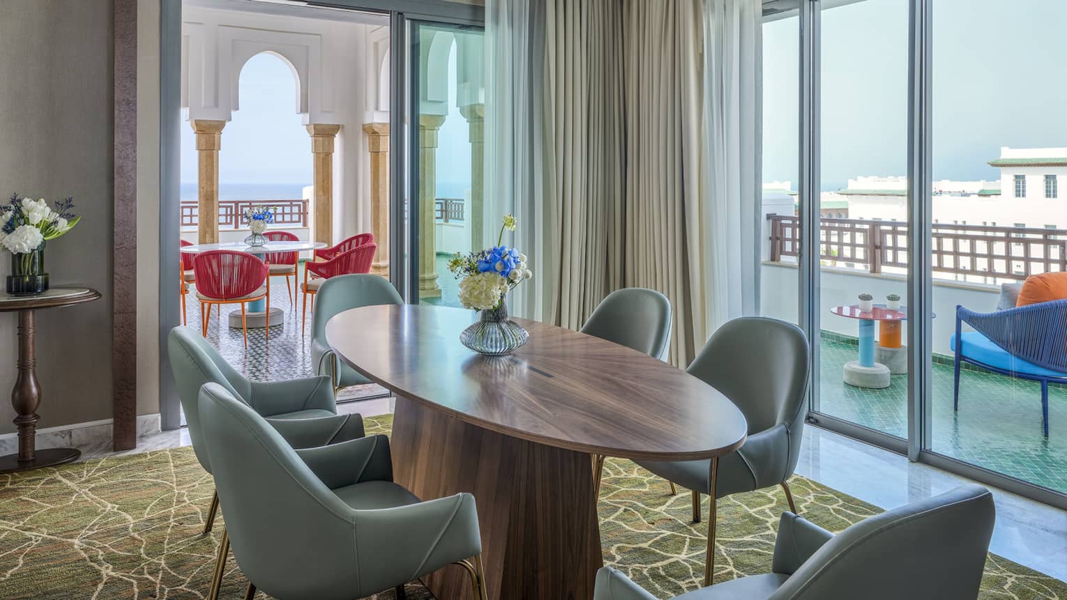 Luxury hotel suite at Four Seasons Hotel Rabat, featuring an oval, wooden dining table with 6 turquoise-coloured chairs and a large terrace