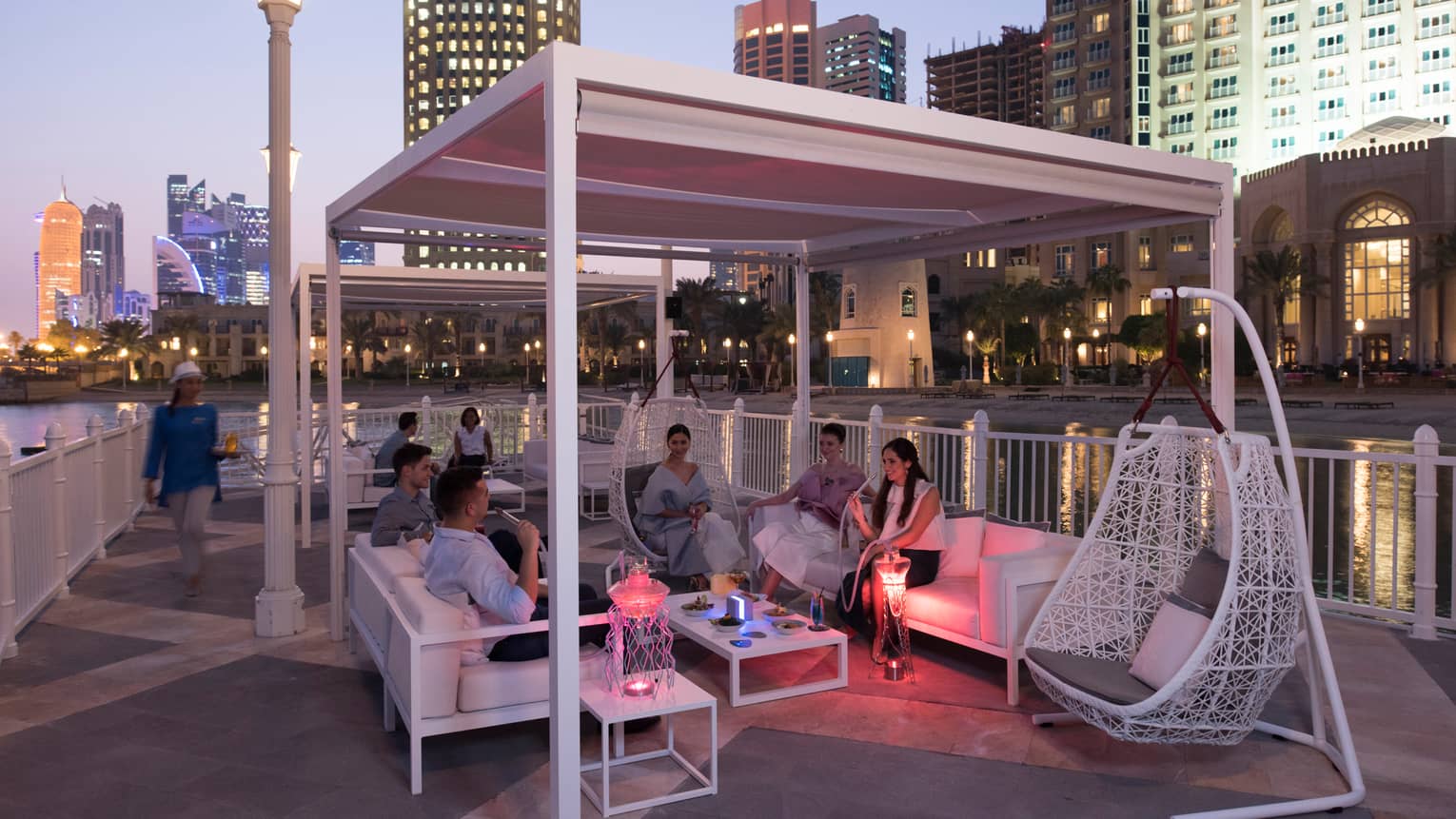 Group of friends in lounge under white pergola on The Pier patio at night