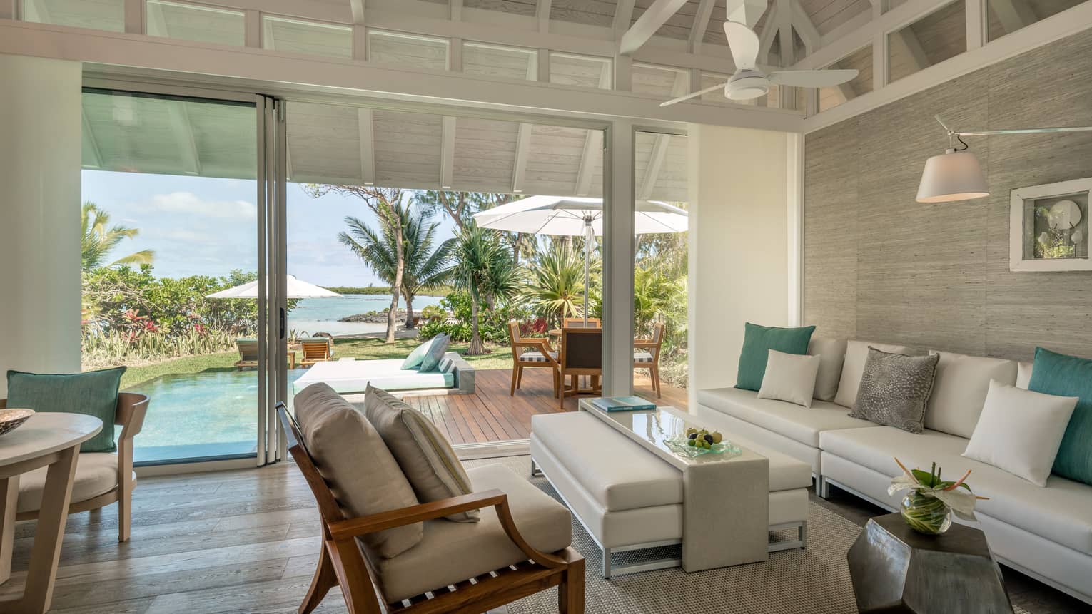 Sanctuary Beach Pool Villa with long white sofa, ottoman, chair, open glass wall to patio