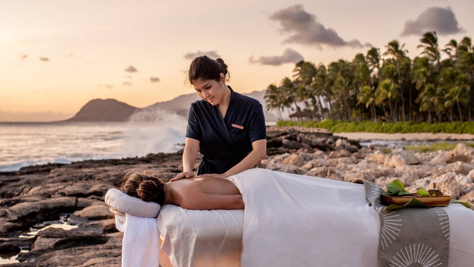 A four seasons guest receives a massage on the beach, as the sun sets in the distance