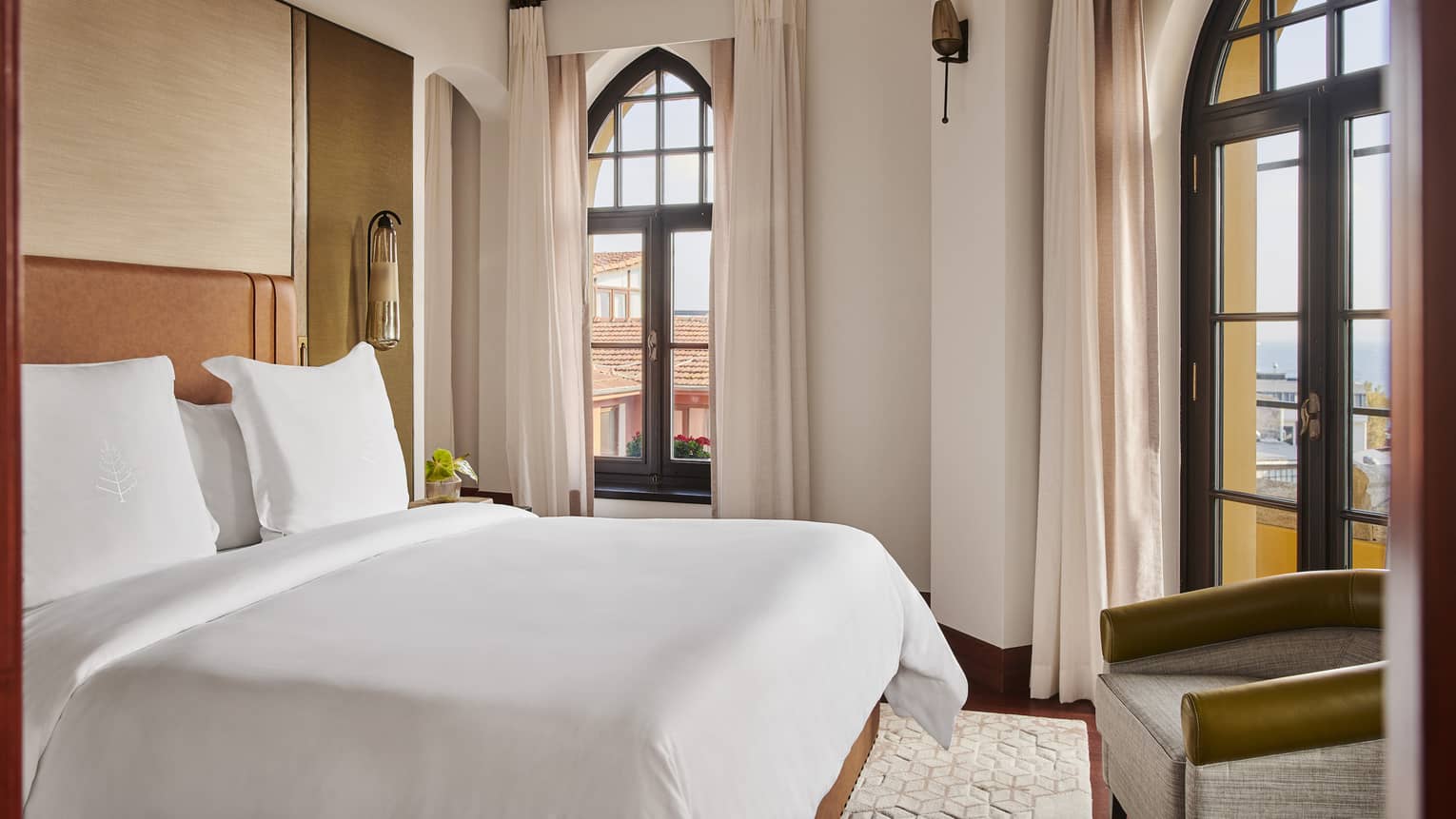White Four Seasons bed, contemporary chair at foot and tall arched windows with long curtains