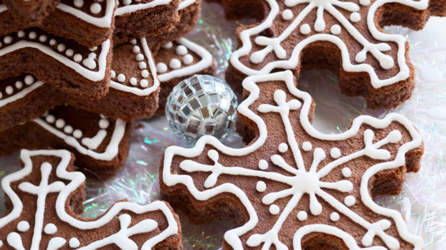 A stack of assorted snowflake-shaped cookies lay decorated with white frosting atop a holiday themed table