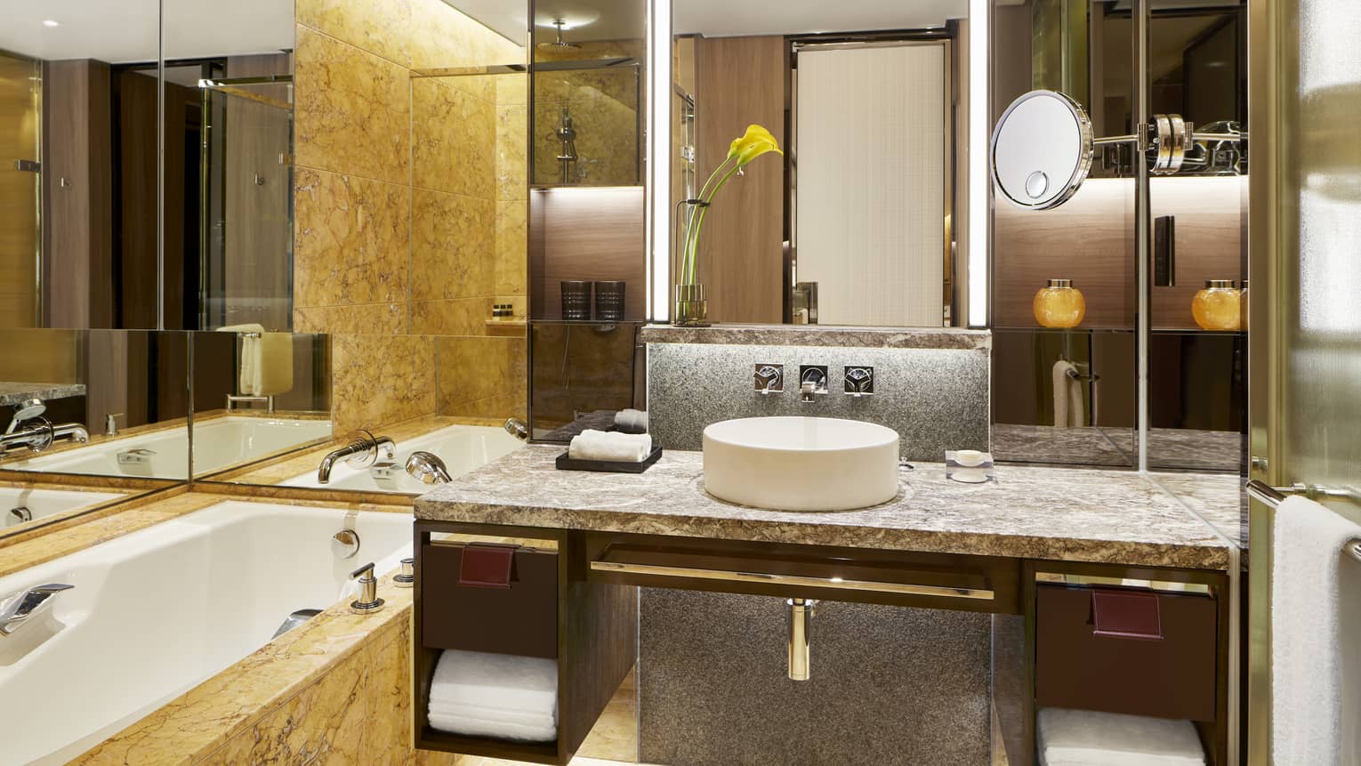 Modern bathroom with a marble countertop, single sink, large mirror, and a bathtub. A yellow flower in a vase decorates the counter.