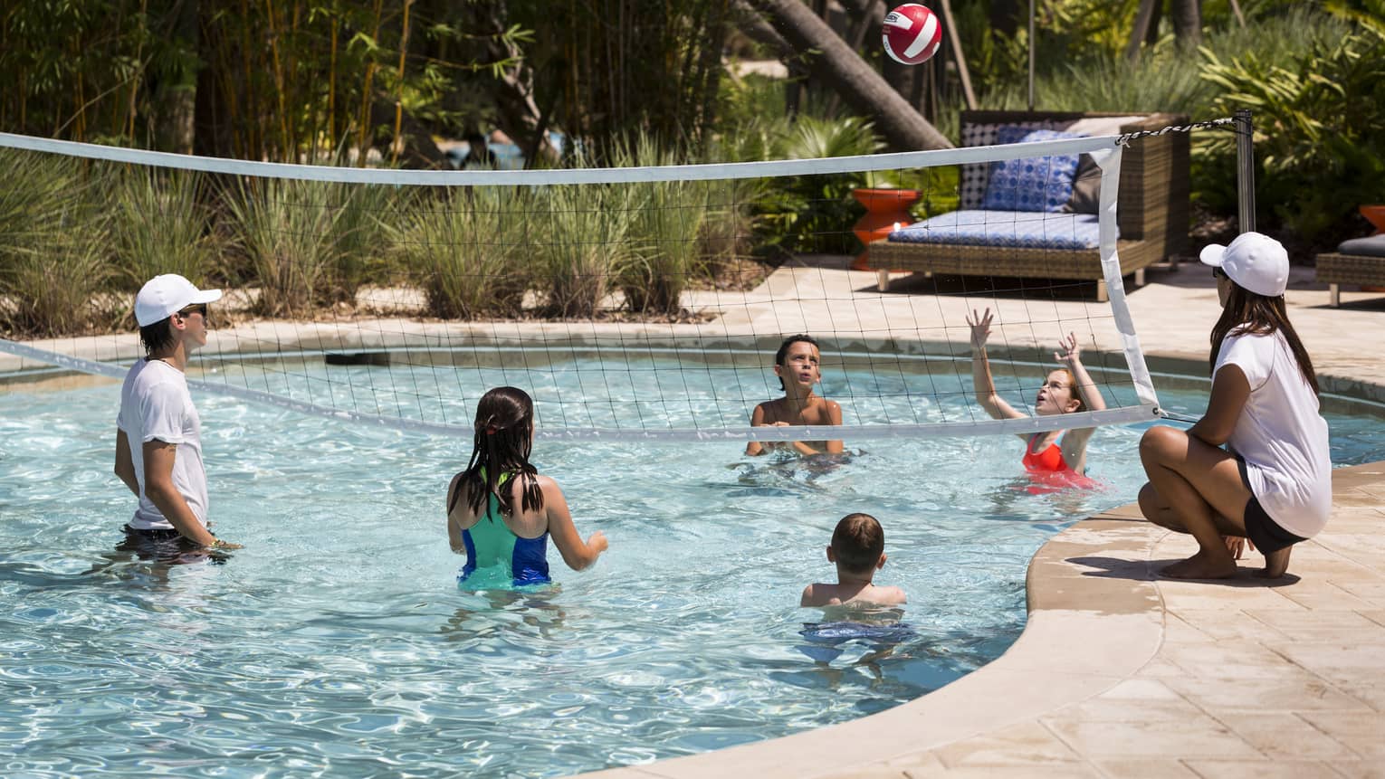 Kids play volleyball in small outdoor swimming pool with net