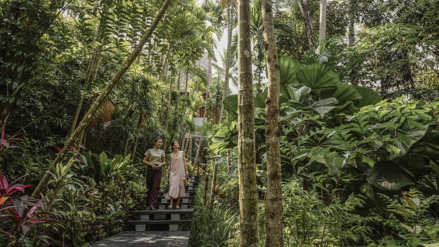 Female guest and spa staff member walk along foliage-lined pathway to the spa