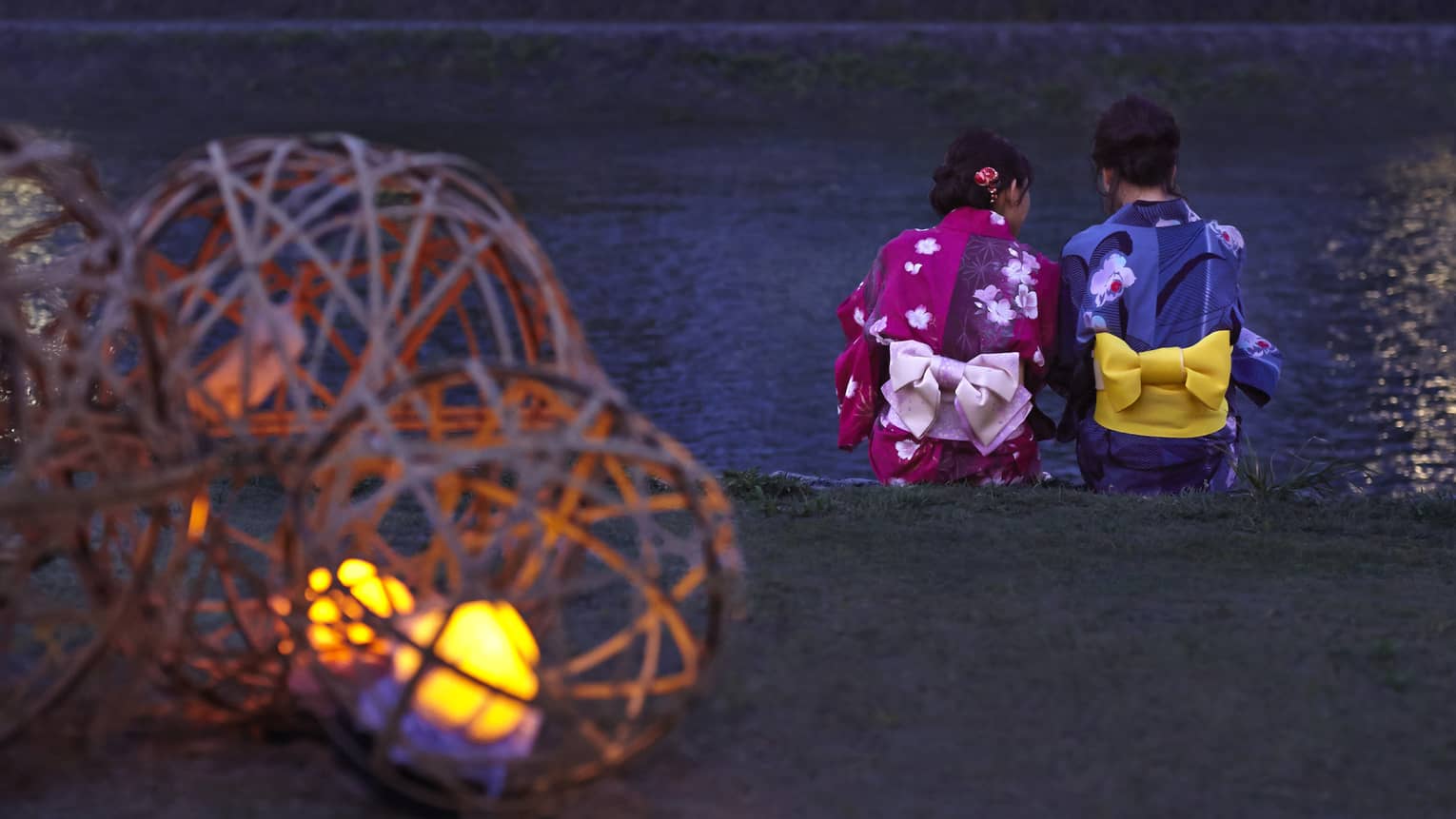 Two Geisha sit on ledge by a river at dusk