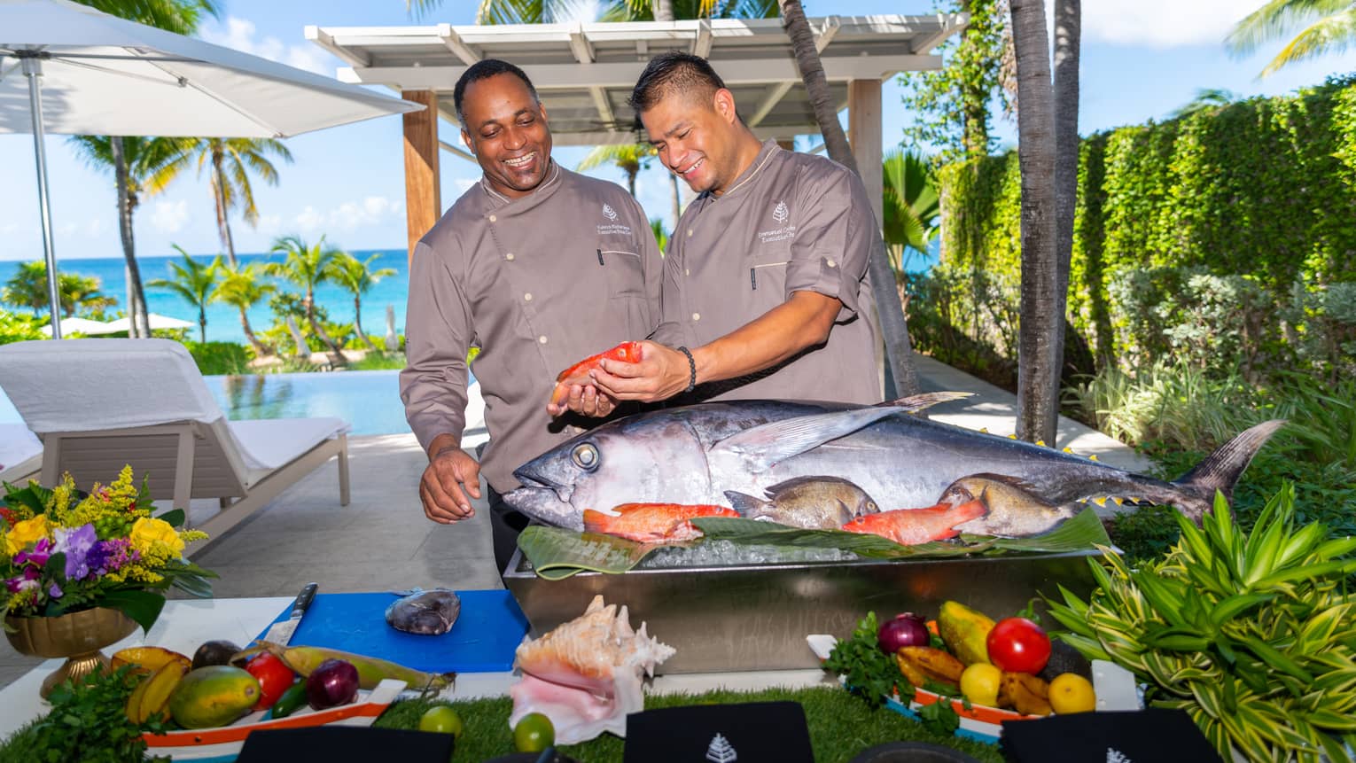 Two people standing in front of a food display with a large fish while holding a smaller fish.