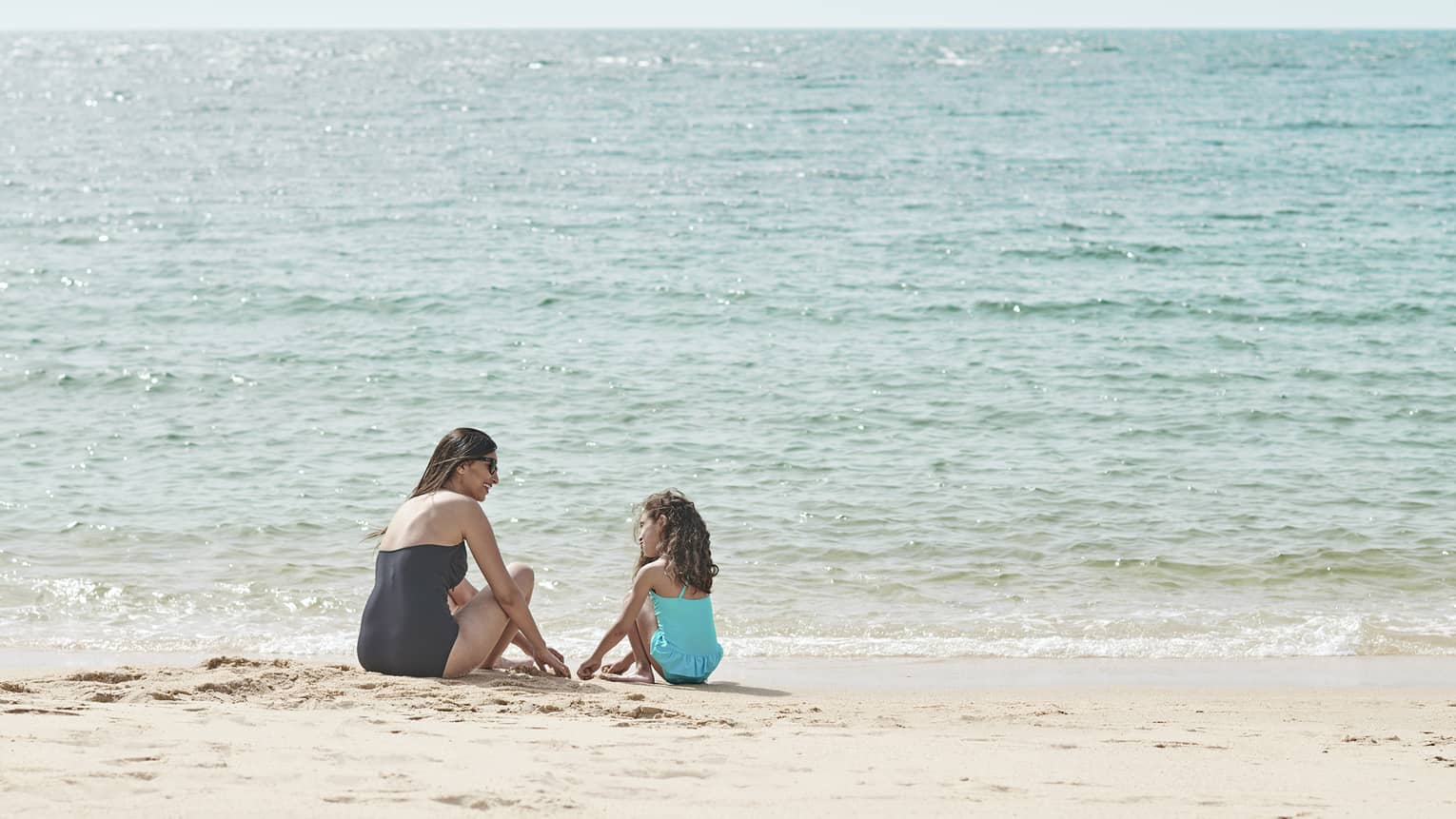 Seated by the water’s edge, a mother and daughter are having fun playing in the sand, while being kissed by the sun’s glow.