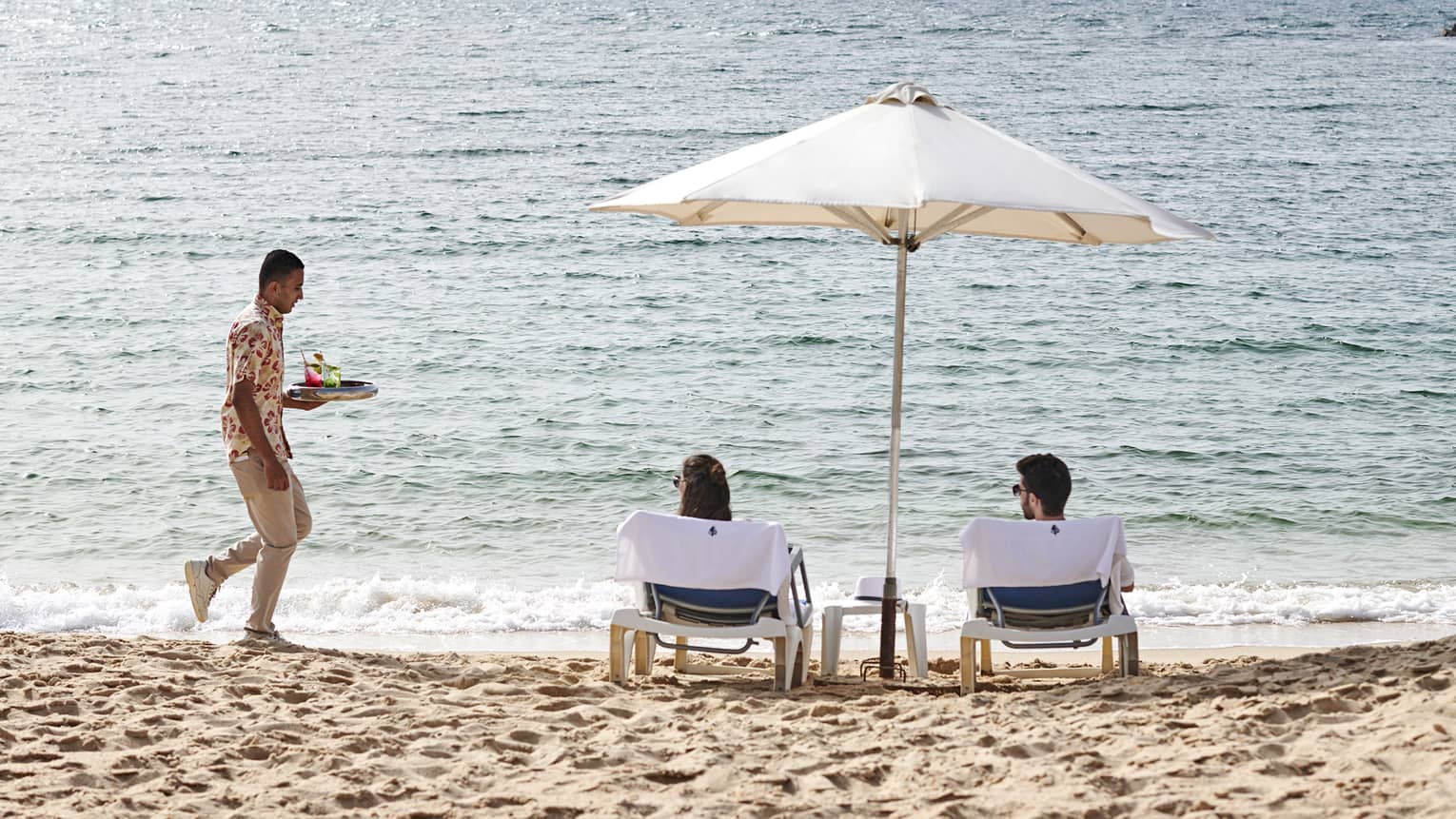 a couple lounges on the beach in alexandria while a four seasons staff serves them refreshments