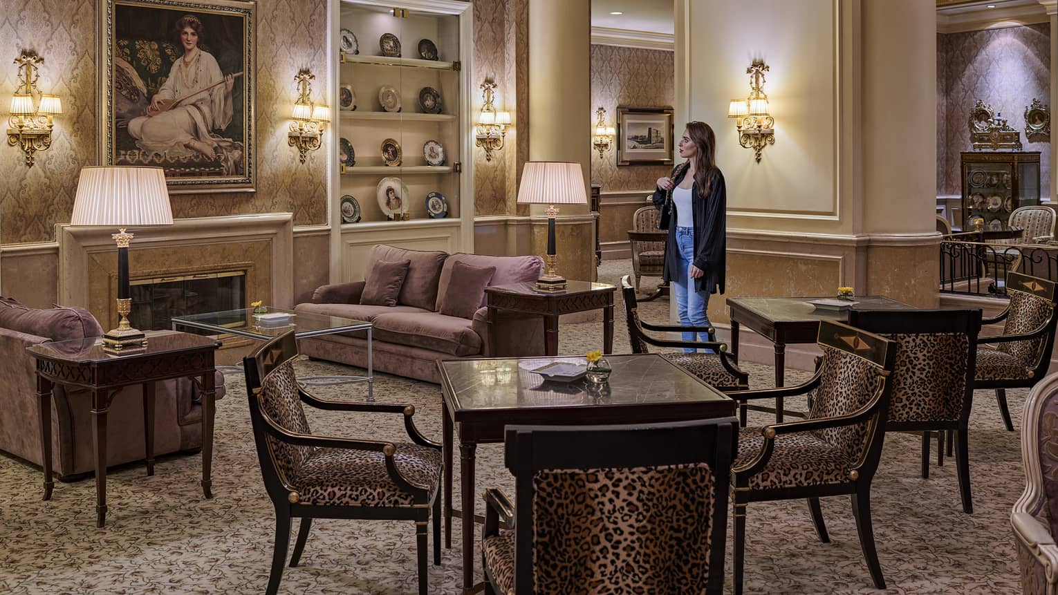 Woman stands in a lounge featuring two dark wood square tables, each with four chairs, two purple sofas