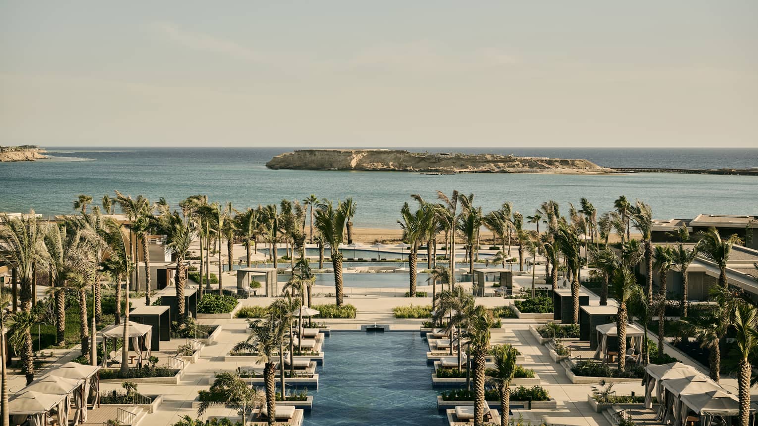 Aerial view of a resort pool with palm trees overlooking sea