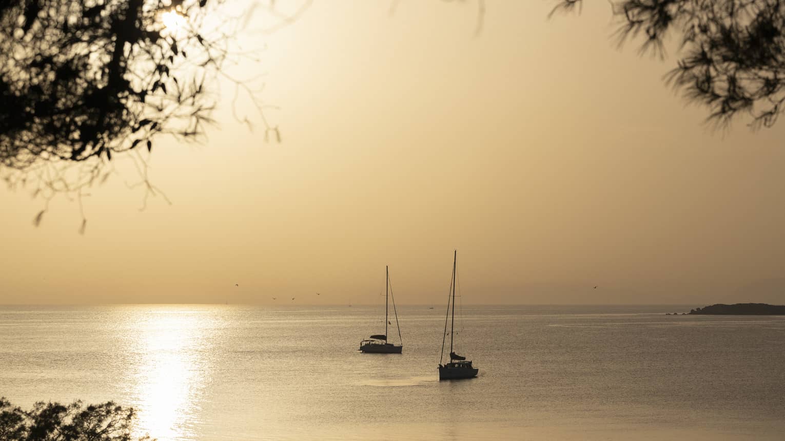 Silhouette of two sailboats at dusk on ocean cruising Greek isles. 