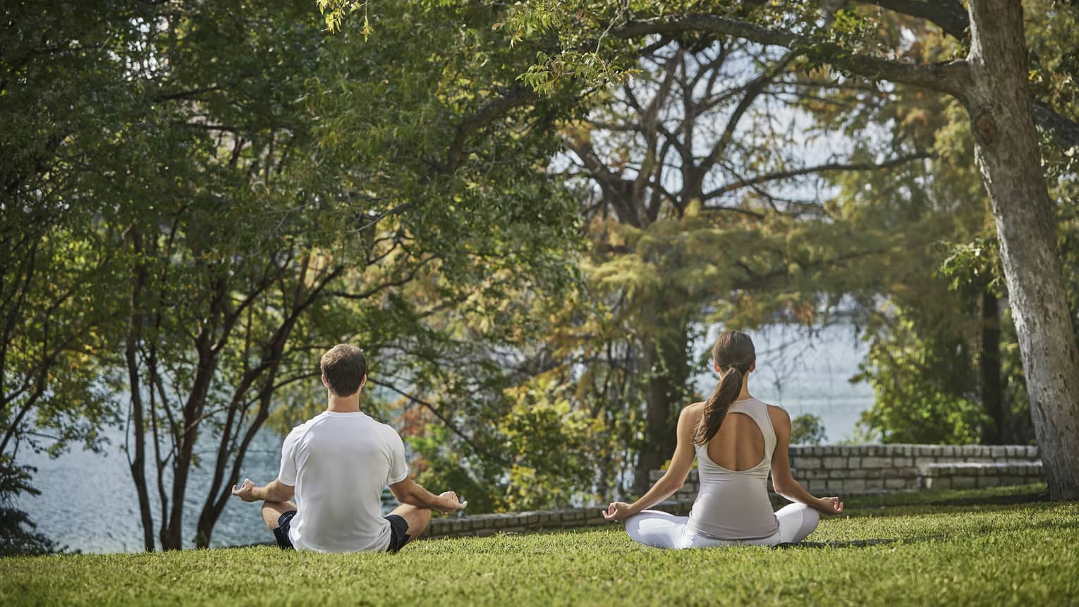 A man and woman in a yoga pose outside near trees.