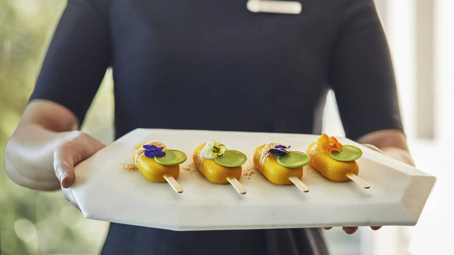 Hotel staff member holding a tray of colorful arrival popsicles 