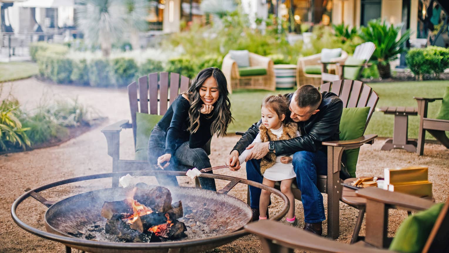 A family roasting marshmallows outside with paths and plants around them.