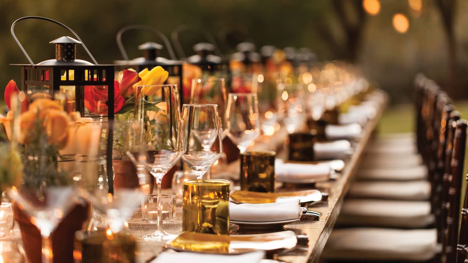 Close-up of long banquet table with red and yellow flower, amber glassware 
