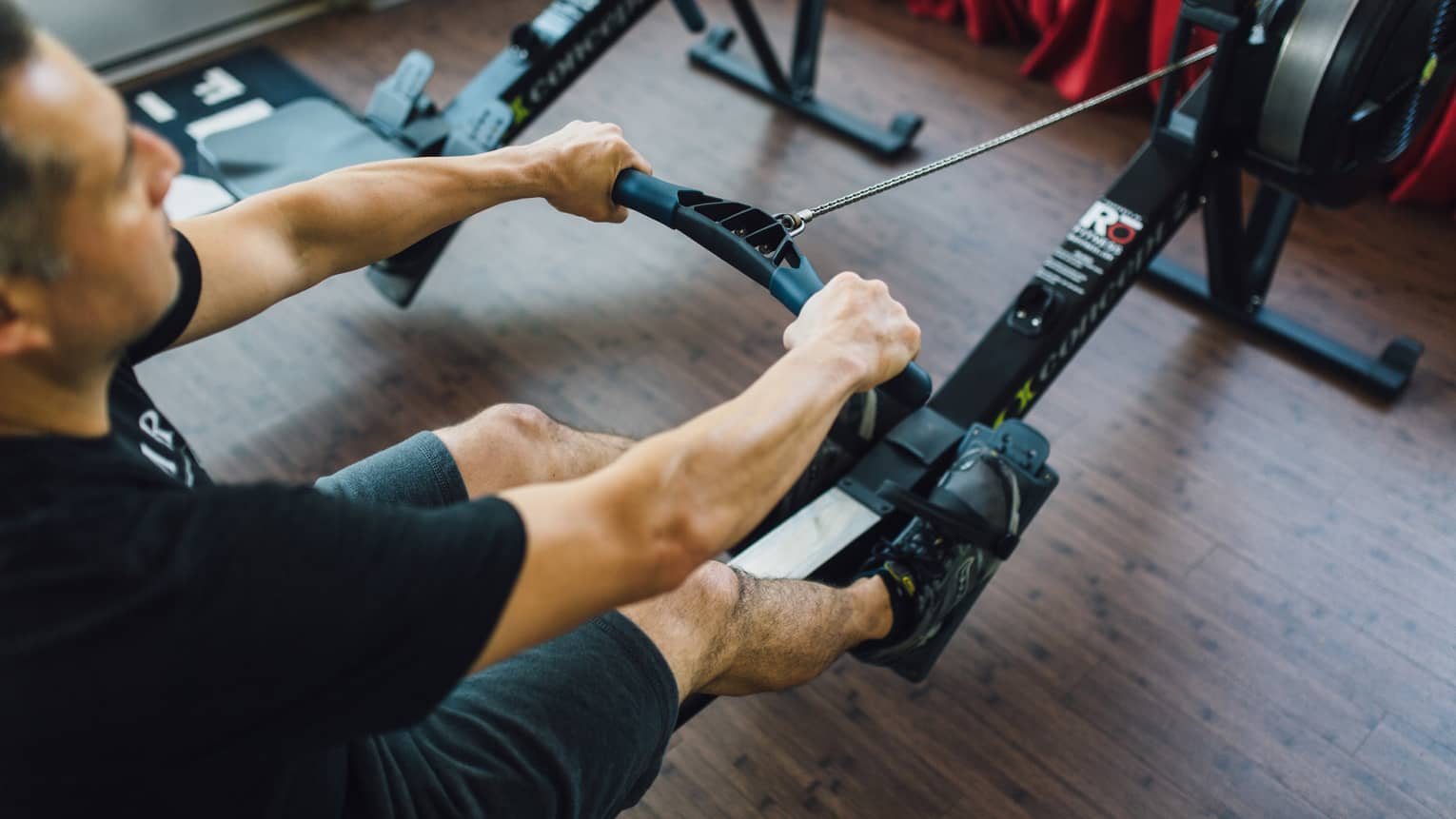 Man sits, pulls handle of cardio rowing machine in fitness facility