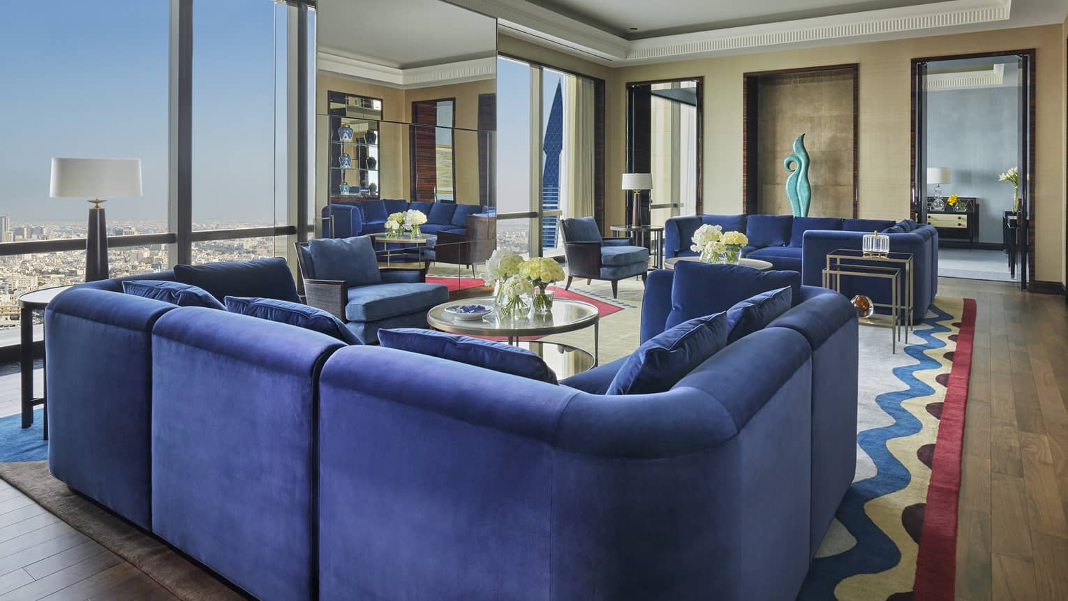Royal Suite large u-shaped blue plush sofa, multiple seating areas, window with Bahrain city views