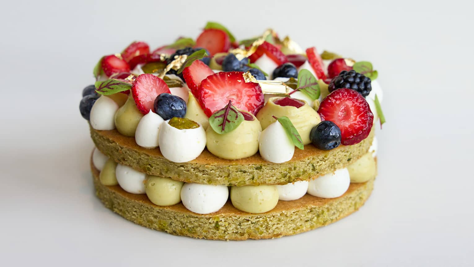 Two-layer pistachio and strawberry cake with pistachio praline, sollops of cream and topped with fresh berries and rose and strawberry marmalade