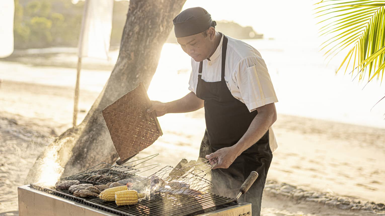Chef grills fresh clams and corn on the cob over a beachside BBQ