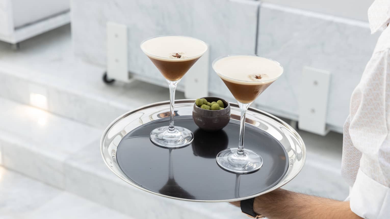 Hotel staff carrying silver tray with two martini cocktails